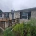 Mobile home with wooden deck, greenery, and overcast sky.