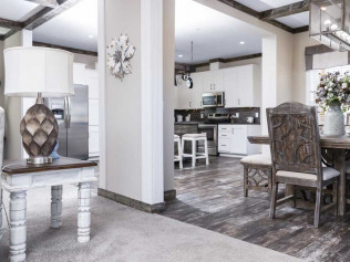 Stylish open-plan kitchen and dining area with white cabinets, a wooden dining table, ornate chairs, and a decorative table lamp, exuding a cozy, modern vibe.
