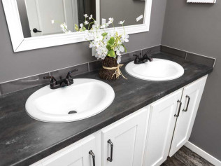 Modern bathroom with gray walls, features a double-sink vanity with white basins and black fixtures. A vase of white flowers adds elegance.