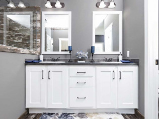 A modern bathroom with a gray color scheme features a double vanity with white cabinets, black countertops, and two mirrors. Blue accents add a calming touch.