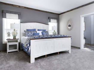 Cozy bedroom featuring a large white bed with blue and white bedding, flanked by lamps on side tables. Grey walls and carpet create a calm, serene atmosphere.