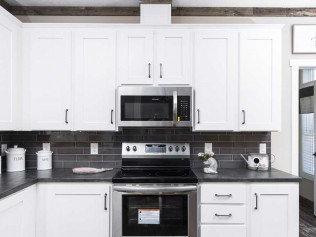 Modern kitchen with white cabinets, dark countertops, and a silver oven and microwave. Black backsplash adds contrast; decor includes canisters and a small plant.