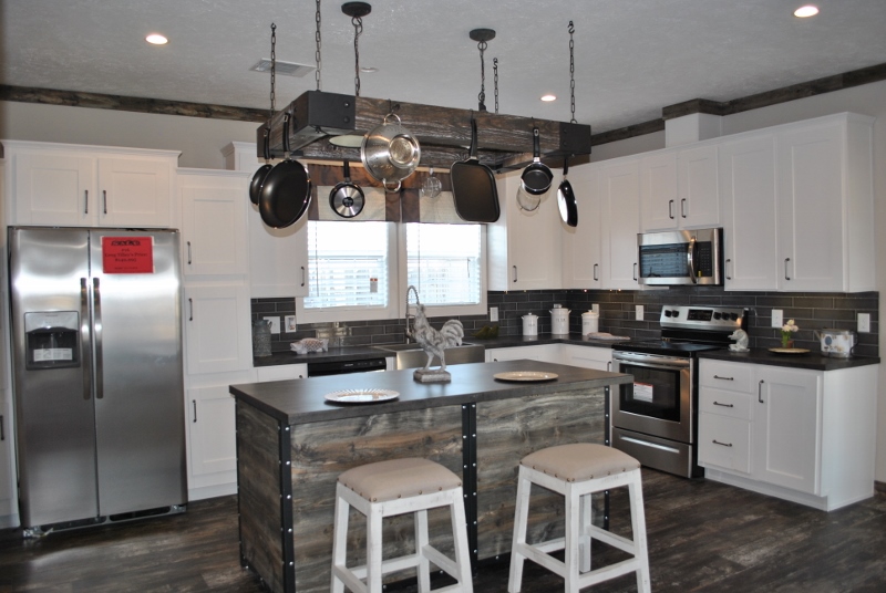 Modern kitchen with white cabinets, stainless steel appliances, and a rustic island with two stools. Pots hang above the island, and a window lets in natural light.