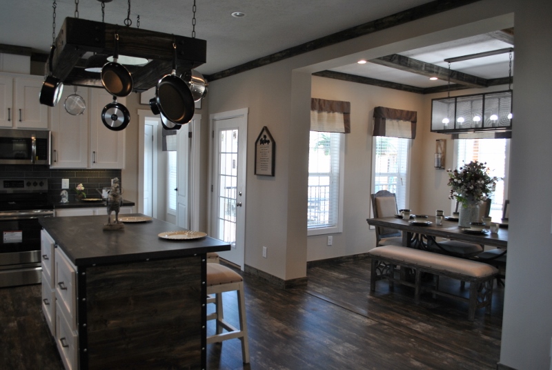 Modern kitchen with dark wood floors, an island with hanging pots, and a cozy dining area. Bright natural light and simple, elegant decor.