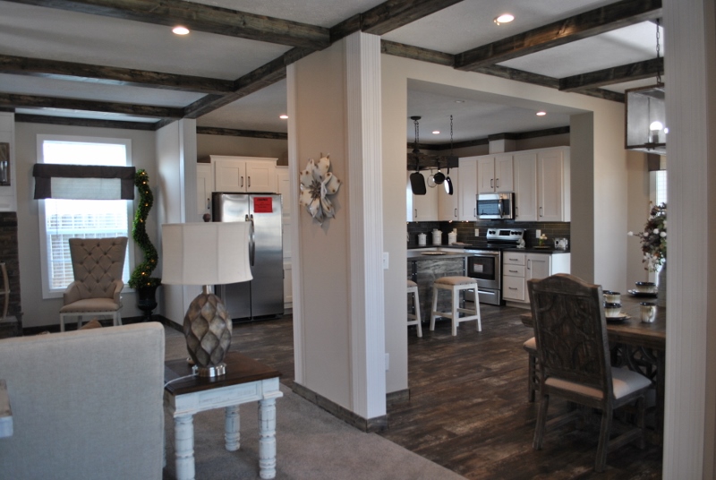 Open-concept kitchen and living area with rustic wood beams. Features white cabinets, stainless steel appliances, and elegant dining space. Warm and inviting tone.