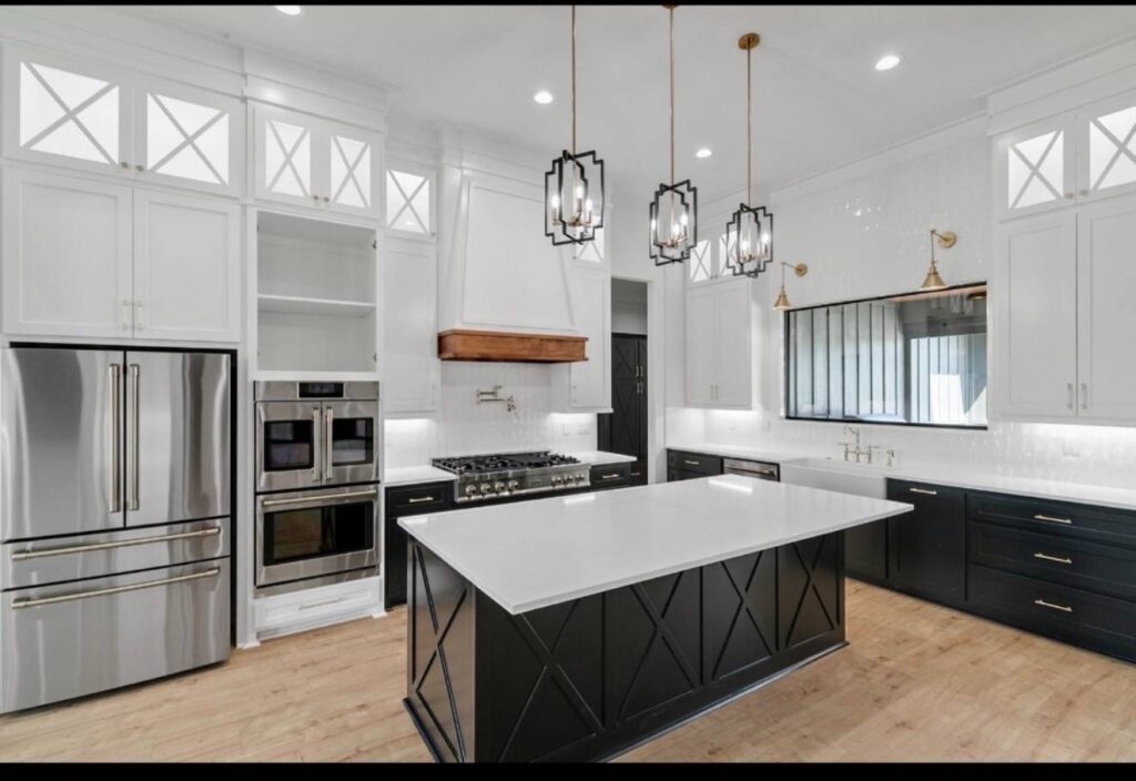 Modern kitchen with white cabinets and black island, wood floor, stainless steel appliances, trio of pendant lights, and elegant, bright atmosphere. Image for illustrative purposes.
