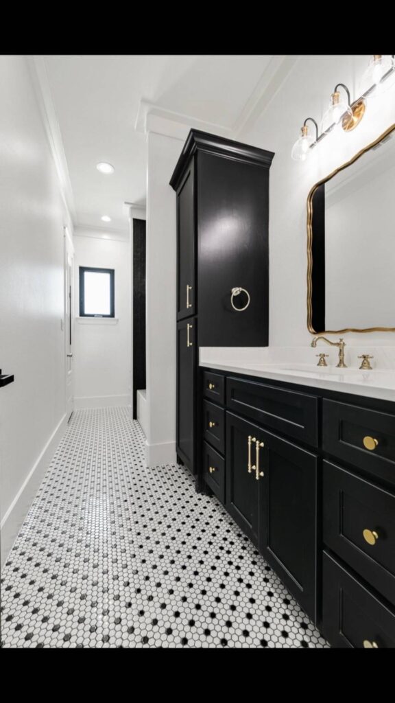 Sleek bathroom with black cabinets and gold hardware. Features a white countertop, elegant mirror, patterned tile floor, and soft lighting.