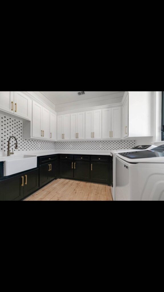 Modern kitchen with white upper cabinets, black lower cabinets, and gold handles. Black and white polka dot backsplash, farmhouse sink, and light wood floor.