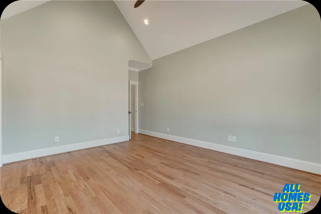 Empty room with light gray walls and high sloped ceiling, featuring warm wooden floors. A white door to the left enhances the open, airy feel. Image for illustrative purposes.