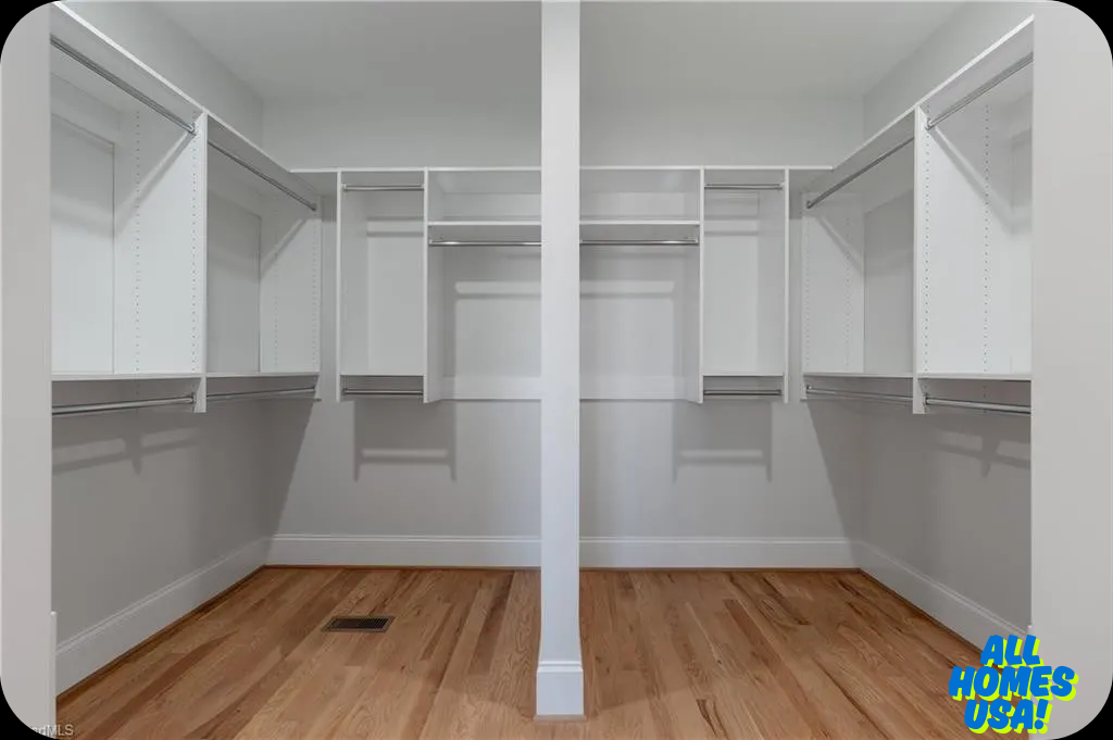 Spacious walk-in closet with hardwood flooring, white walls, and organized shelving on three sides. Bright and clean with a minimalist design. Image for illustrative purposes.
