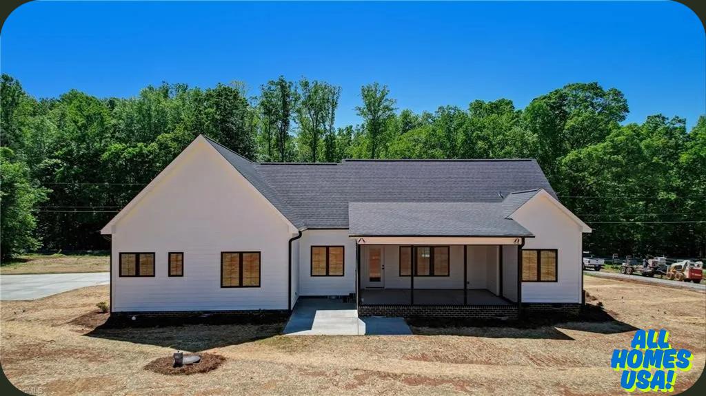 A modern white house with dark trim sits against a backdrop of dense green trees under a clear blue sky. The yard is a mix of dirt and sparse grass. "All Homes USA" is in the bottom right corner. Image for illustrative purposes.