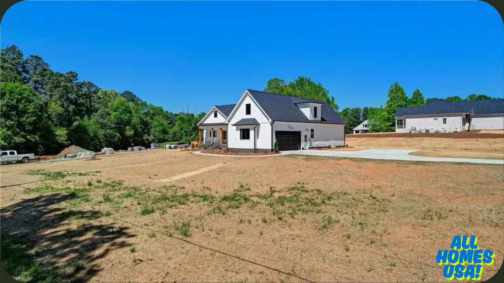 A newly built white house with a dark roof sits on a large, open plot of land with sparse grass. Surrounding trees and clear blue sky create a serene backdrop. Image for illustrative purposes.