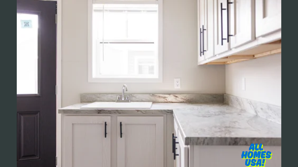 Bright kitchen with white cabinets, granite countertops, and a stainless steel sink under a window. Black door on the left. Clean and modern design. Image for illustrative purposes.
