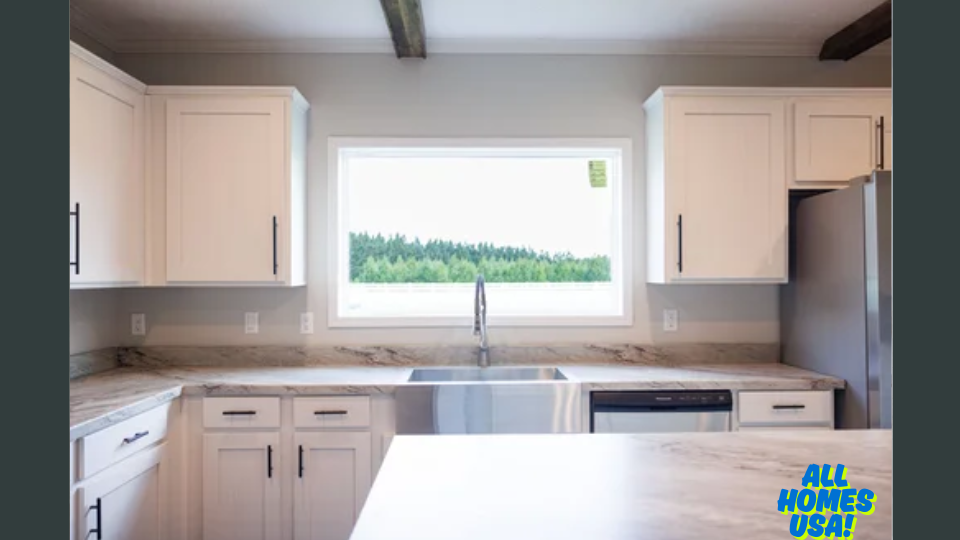 Modern kitchen with white cabinets and marble countertops. A large window above the sink overlooks a green forest, creating a serene ambiance. Logo in bottom right. Image for illustrative purposes.