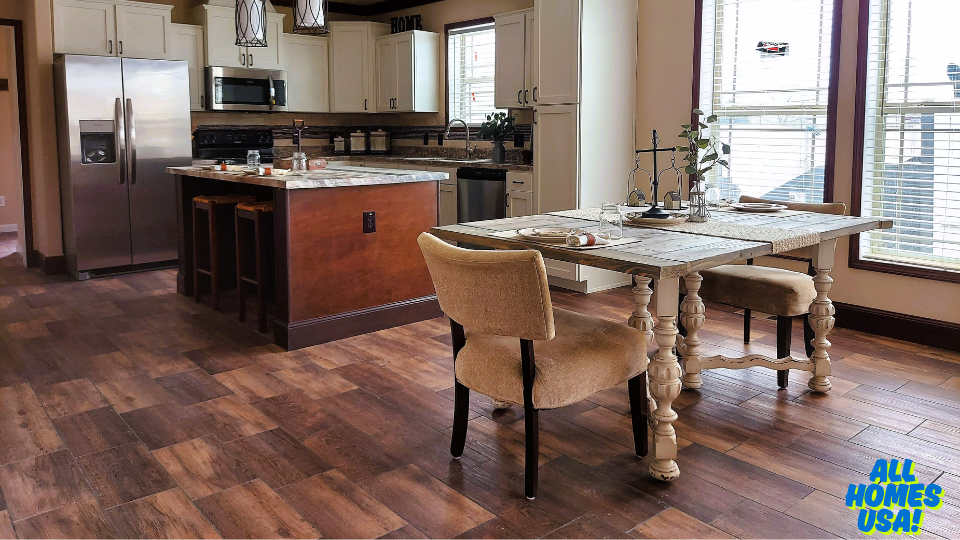 A modern kitchen and dining area with wooden flooring. The kitchen features white cabinets, a steel fridge, and an island with stools. The dining table has elegant chairs and is set for a meal, creating a cozy and inviting atmosphere. Bright windows with blinds allow natural light. Image for illustrative purposes.